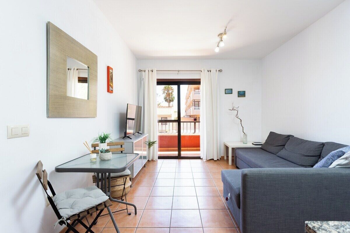 A compact living space with a dining table, a sofa, a TV, and a balcony with a view of buildings.
