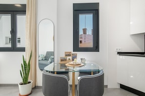 A modern kitchen with white cabinets, a glass dining table, and a potted plant. - Apartment 'Cervantes Homes No1' with Shared Terrace, Wi-Fi and Air Conditioning (Conil de la Frontera)