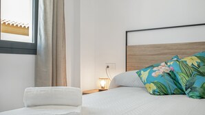 Ein ordentlich bezogenes Bett mit einem floralen Kissen, einem gefalteten weißen Handtuch und einer Nachttischlampe.