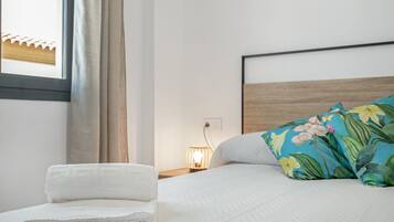 A neatly made bed with a floral pillow, a folded white towel, and a bedside lamp.