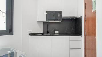 A modern kitchen with white cabinets, a black countertop, a microwave, and a sink.