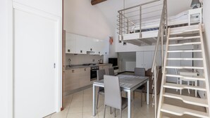 A compact kitchen with modern appliances, a dining area with a table and chairs, and a loft bedroom with a ladder. - Cozy Mezzanine Apartment by Wonderful Italy (Bologna)