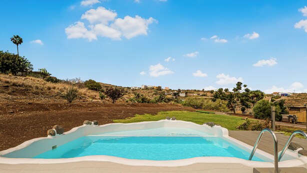 A swimming pool with a wooden deck, surrounded by a hilly landscape and clear blue sky.