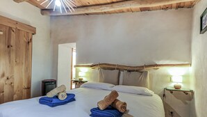 A bedroom with a wooden ceiling, a bed with white linens, and two nightstands with lamps.