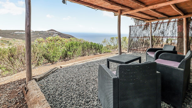 Un espacio de estar al aire libre cubierto con mobiliario de mimbre y vistas al mar.