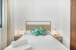 Una cama bien hecha con cabecera de madera, dos mesitas de noche con lámparas y una ventana con cortinas.