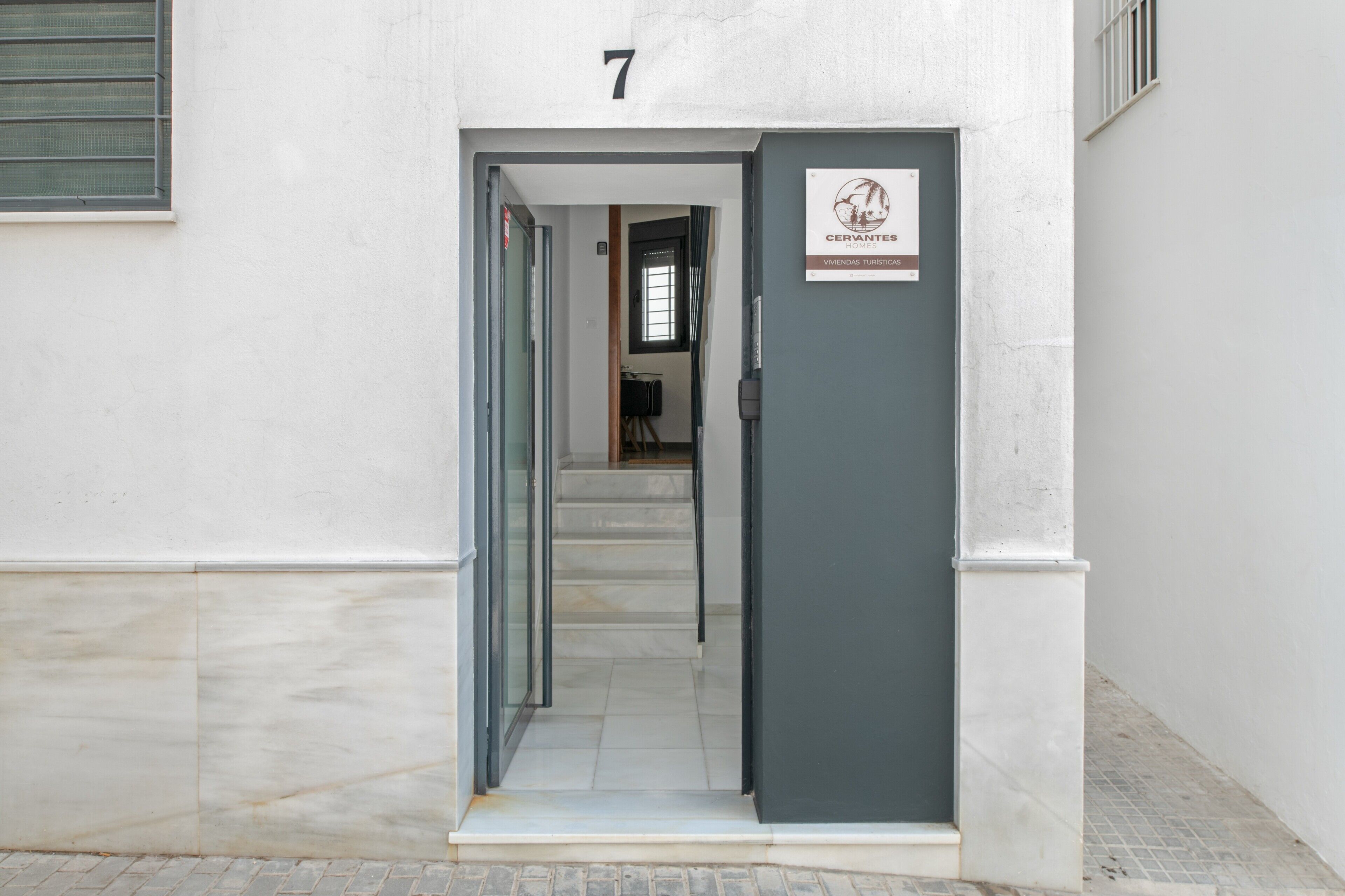A building entrance with a door marked '7' and a sign indicating 'CERRANTES - VIVIENDA TURISTA.'