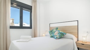 A neatly made bed with a pillow, a bedside table with a lamp, and a window with curtains. - Apartment 'Cervantes Homes No3' with Shared Terrace, Wi-Fi and Air Conditioning (Conil de la Frontera)