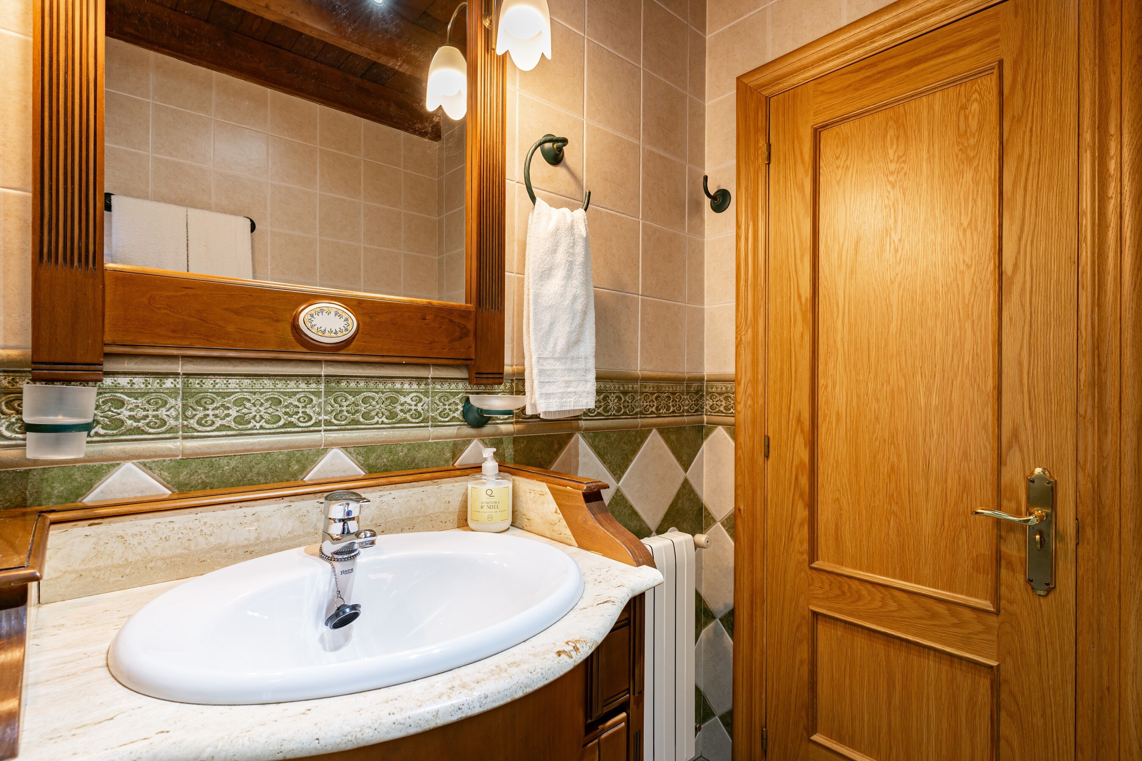 Un baño con puerta de madera, un lavabo con espejo y una toalla colgada de un gancho.