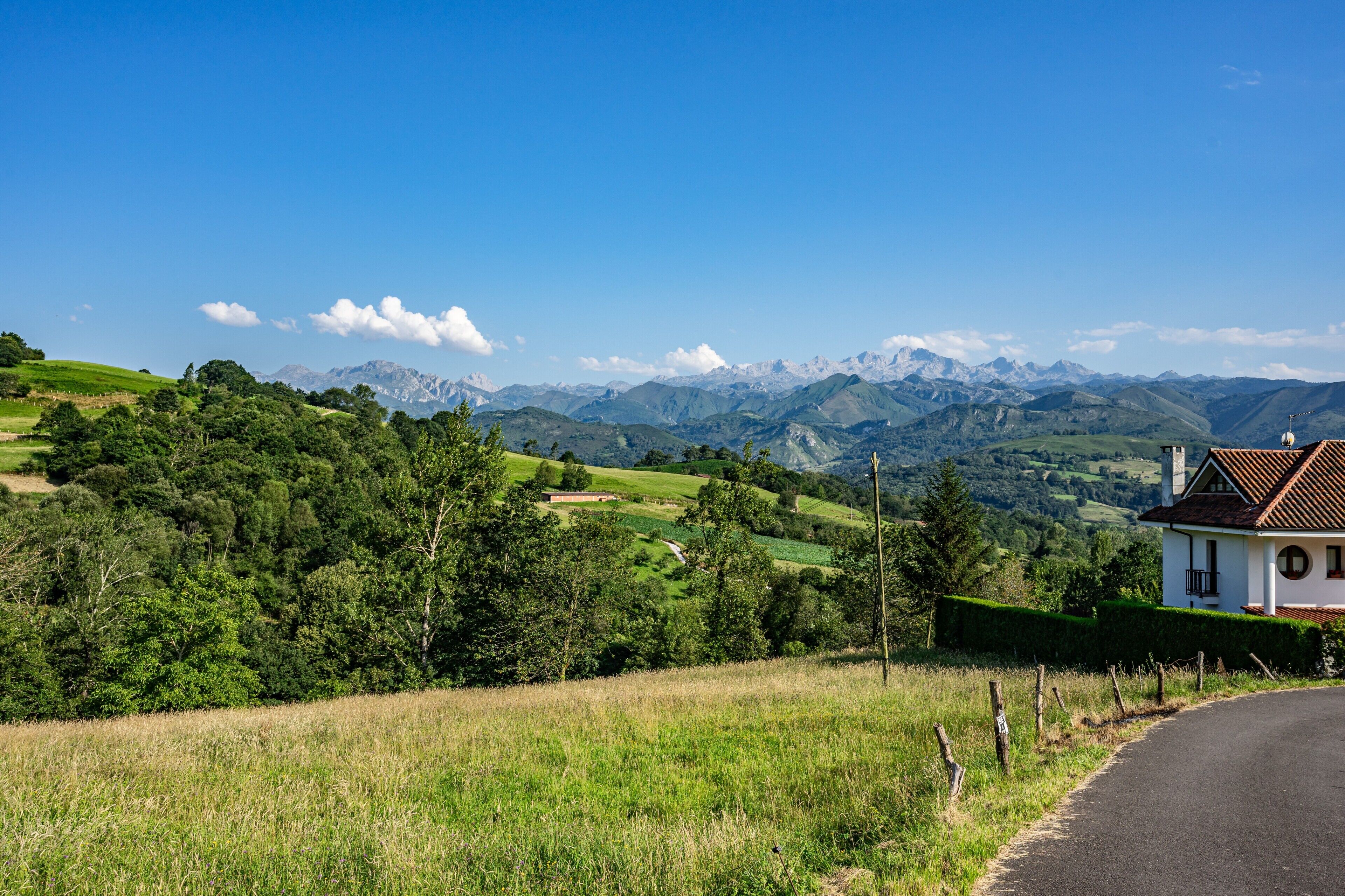 A rural landscape with a house, green fields, and distant mountains.