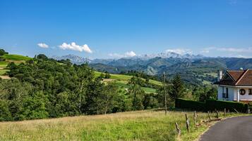 Paisaje rural con una casa, campos verdes y montañas a la distancia.