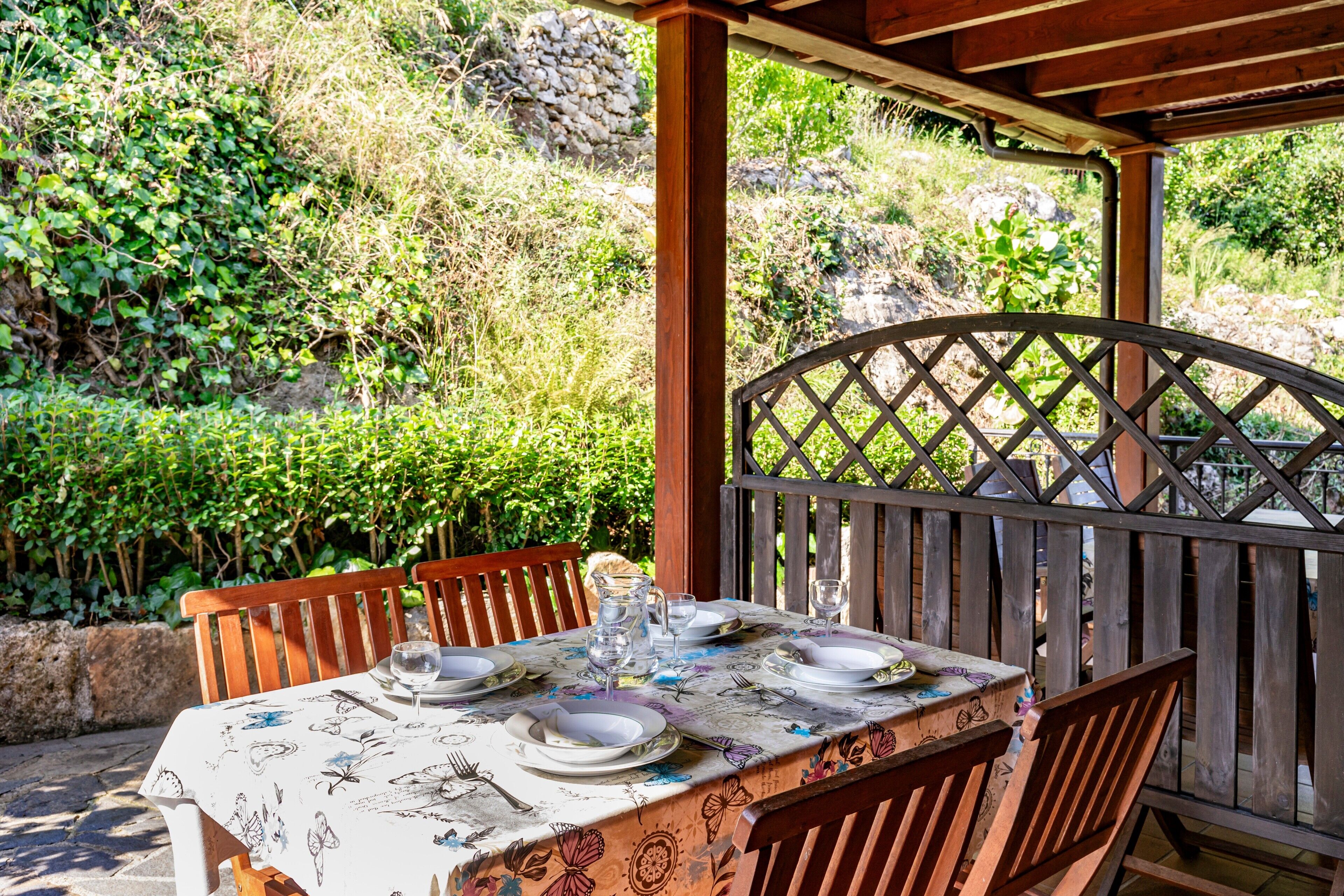 Een eettafel met stoelen, een houten pergola en uitzicht op groen.