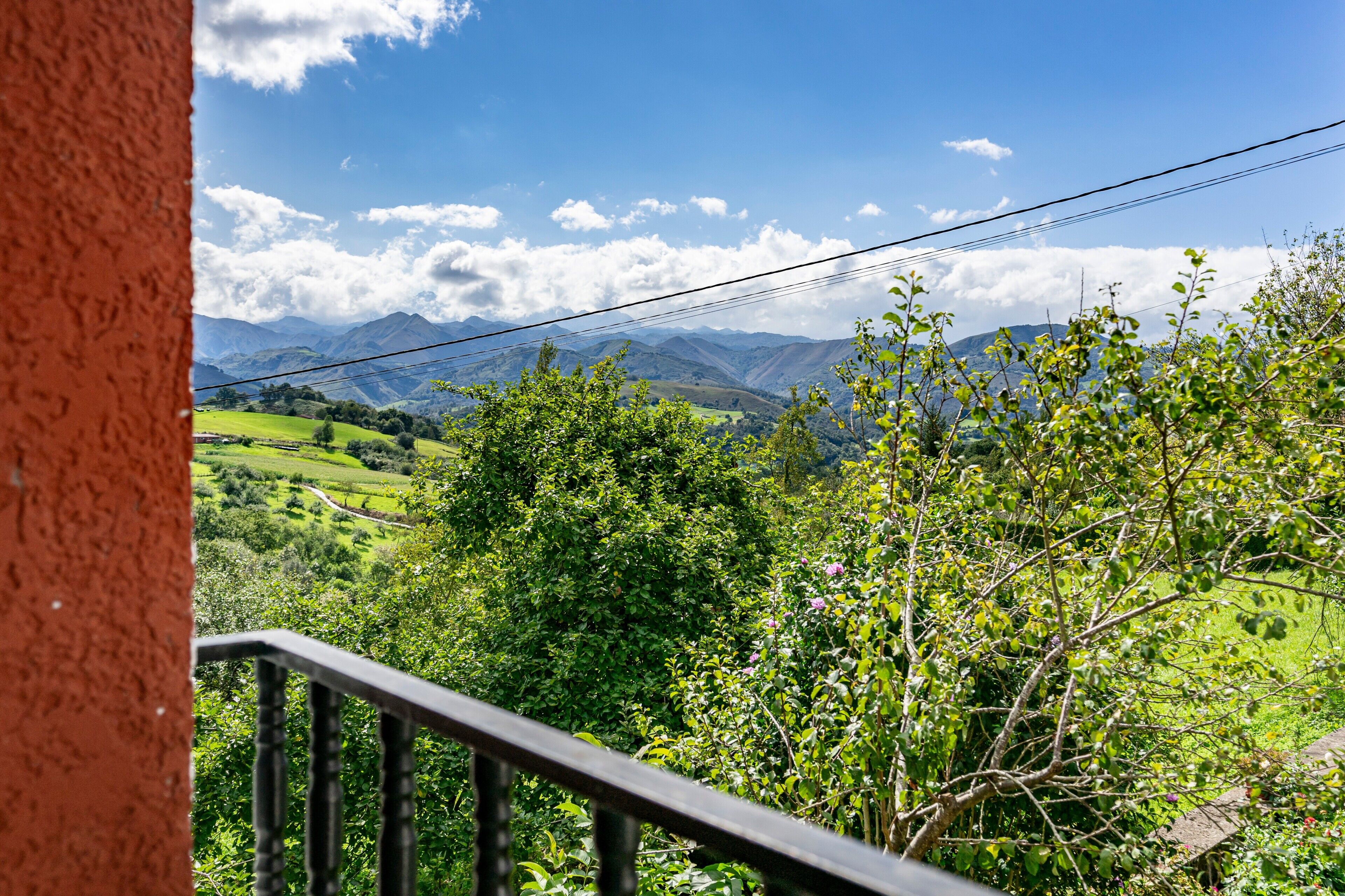Ein Balkon mit Blick auf grüne Felder, Berge und einen klaren Himmel.