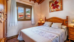 Ein Schlafzimmer mit einem hölzernen Bett, einem Fenster mit Vorhängen, einem Nachttisch mit Lampe und einem Wandbild.