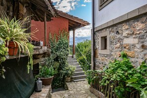 Una escalera de piedra que conduce a una puerta de madera, rodeada de vegetación y un edificio rojo.