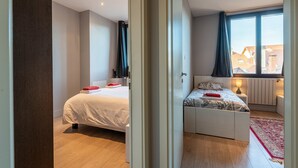 A bedroom with two beds, a window with curtains, a radiator, and a wooden floor. - Apartment 'Annecy - Le 10' with Balcony, Wi-Fi and Air Conditioning (Annecy)