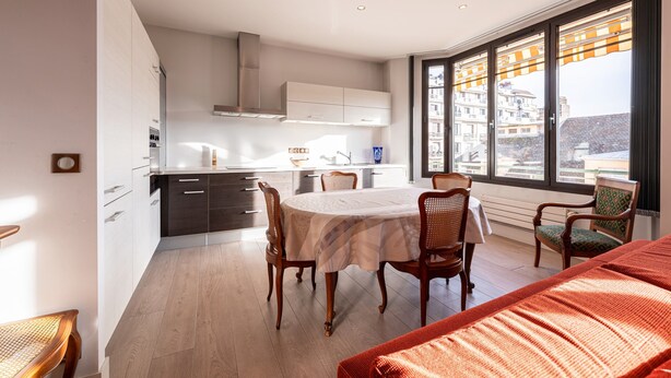A modern kitchen with white cabinets, a dining table with chairs, and a large window with a view of buildings. - Apartment 'Annecy - Le 10' with Balcony, Wi-Fi and Air Conditioning (Annecy)