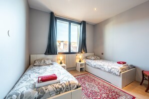 Une chambre avec deux lits, une fenêtre avec des rideaux, un tapis rouge et une chaise.
