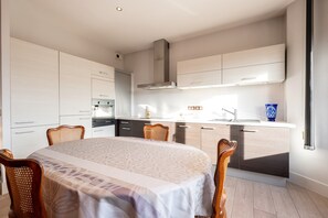 Une cuisine moderne avec des meubles blancs, un four encastré et un coin repas comprenant une table et des chaises.