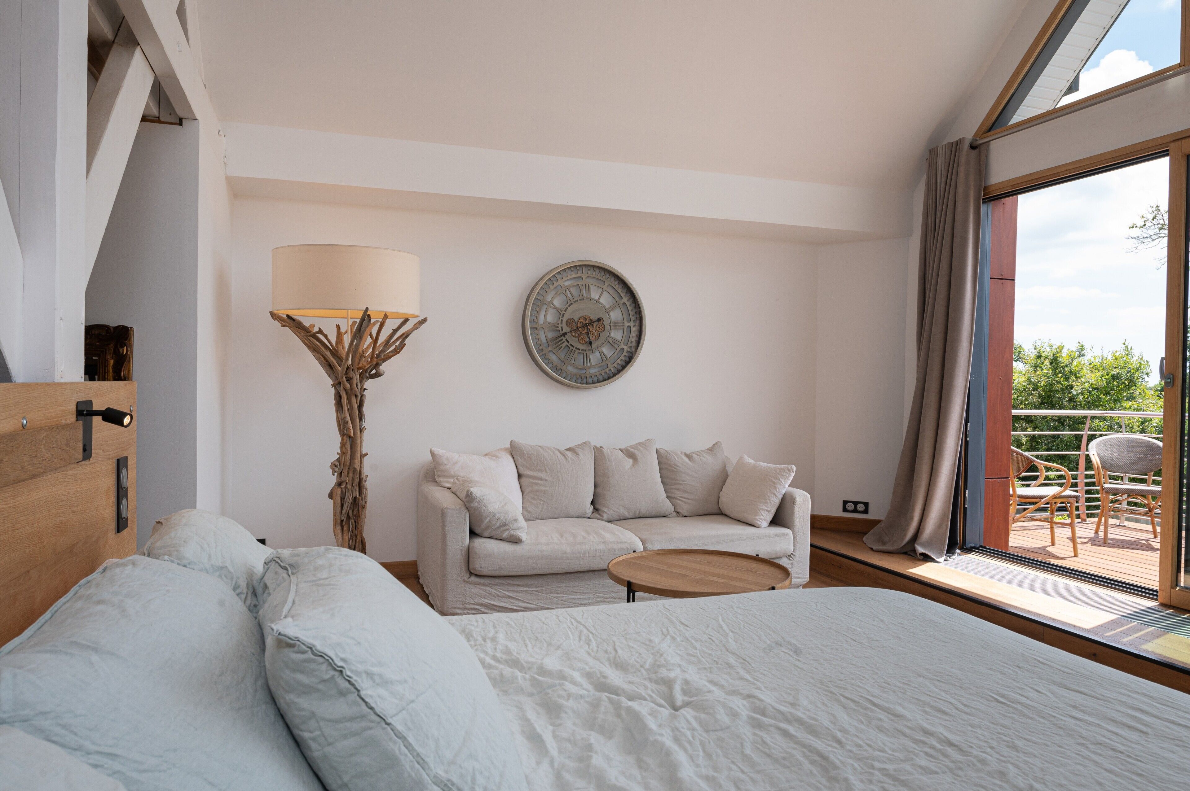 Un dormitorio con cama, sofá, una mesita de centro, una lámpara y un reloj en la pared.