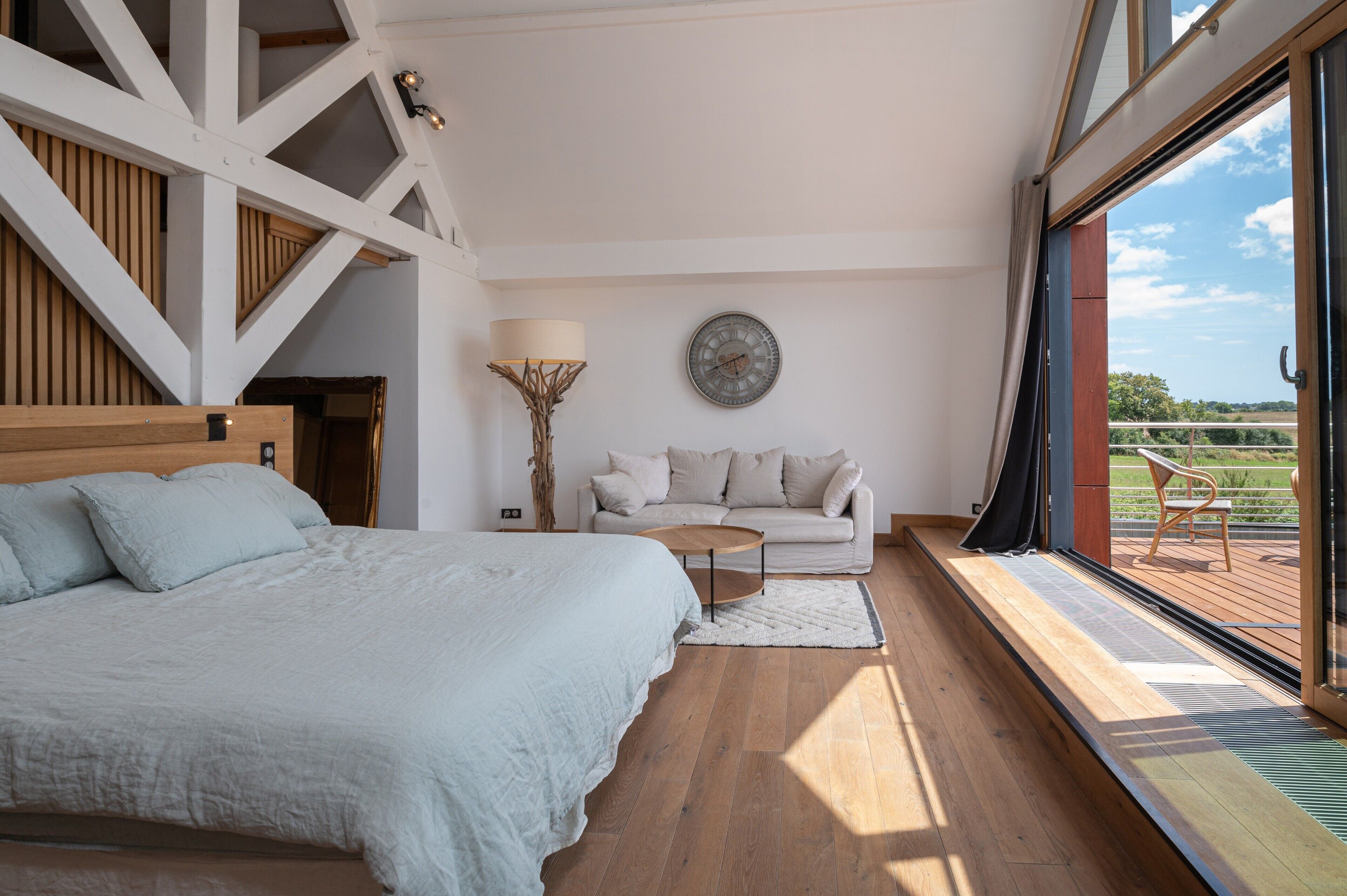 A bedroom with a large bed, a sofa, a small table, and a view of the outdoors through a large window.