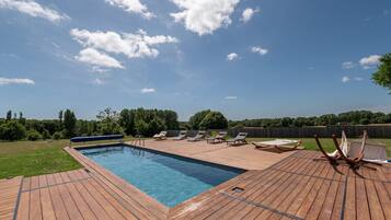 Une piscine rectangulaire avec une terrasse en bois, entourée de chaises longues et d’une clôture en bois.