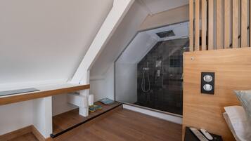 Une chambre moderne avec un plafond en pente, une cabine de douche en verre, un bureau en bois et un lit doté d’une tête de lit.