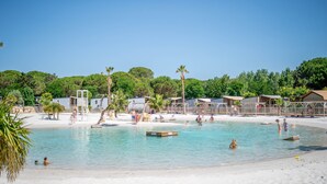 A beach resort with clear blue water, palm trees, and beach huts. - Caravan 'Valras Plage 5 Étoiles' with Shared Pool, Wi-Fi and Air Conditioning (Vendres)