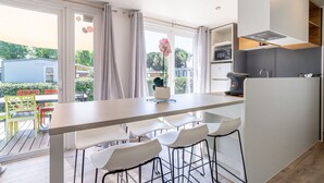 A modern kitchen with a large island, bar stools, and a view of the outdoors. - Caravan 'Valras Plage 5 Étoiles' with Shared Pool, Wi-Fi and Air Conditioning (Vendres)