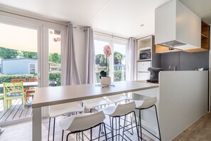 A modern kitchen with a large island, bar stools, and a view of the outdoors. - Caravan 'Valras Plage 5 Étoiles' with Shared Pool, Wi-Fi and Air Conditioning (Vendres)