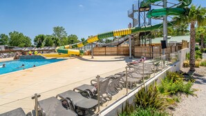 A pool area with a water slide, lounge chairs, and a palm tree. - Caravan 'Valras Plage 5 Étoiles' with Shared Pool, Wi-Fi and Air Conditioning (Vendres)