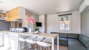 A modern kitchen with a dining area, a sofa, and a TV. - Caravan 'Valras Plage 5 Étoiles' with Shared Pool, Wi-Fi and Air Conditioning (Vendres)