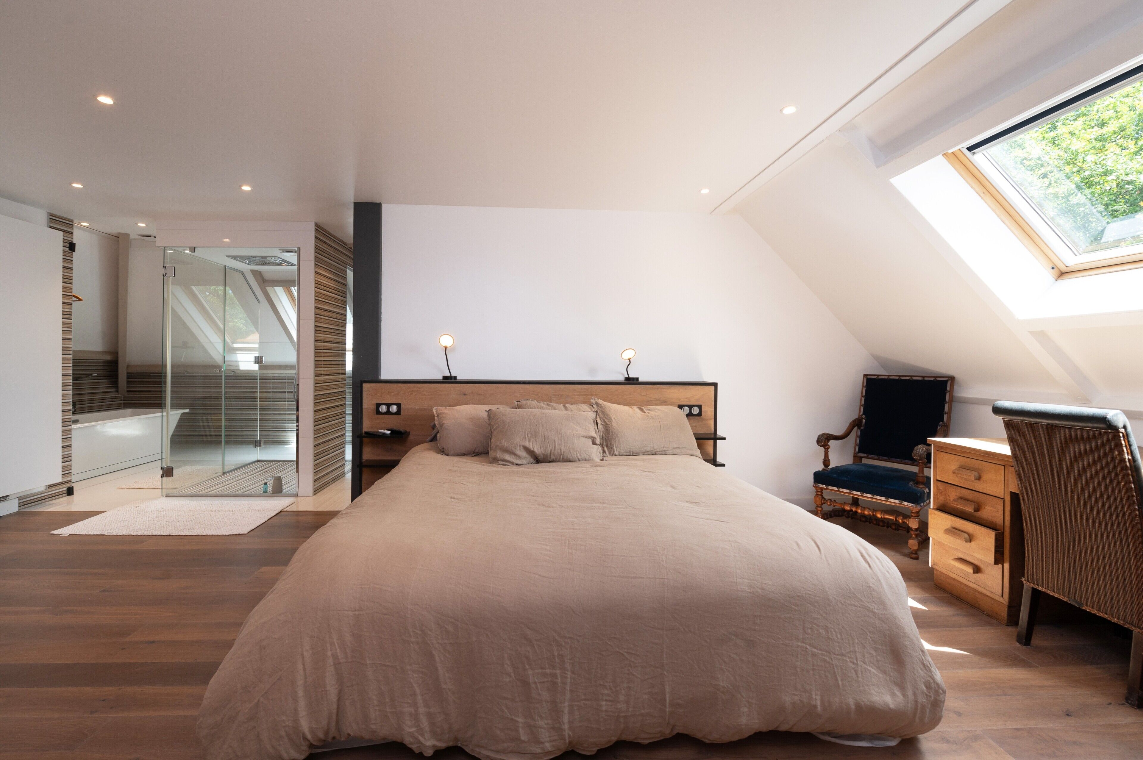 Une chambre dotée d’un grand lit, d’un bureau, d’une chaise, d’une lucarne et d’une porte vitrée donnant sur un balcon.