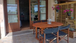Una mesa y sillas de madera en un patio soleado con vistas a través de puertas de cristal.