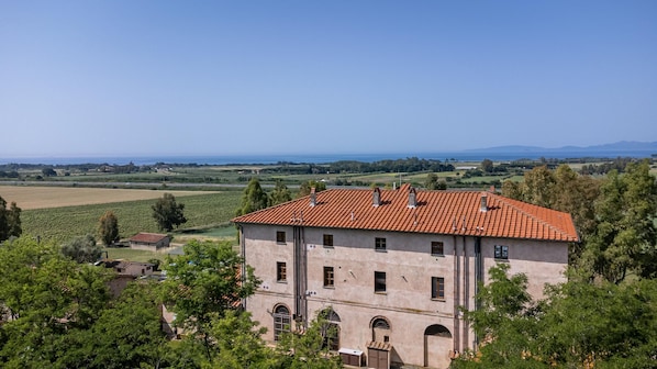 A large building with a red-tiled roof, arched windows, and a view of a vineyard and distant mountains.