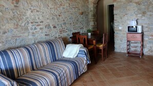 Una habitación con pared de piedra, un sofá a rayas, una mesa de comedor con sillas y un microondas sobre un carrito.