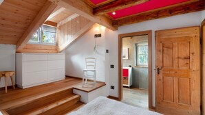 Une chambre avec un plancher en bois, un lit, une chaise blanche, une petite table et un escalier menant à un niveau supérieur.