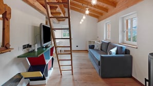 Une pièce avec un plafond en bois, une télévision, un canapé, une échelle et une fenêtre.