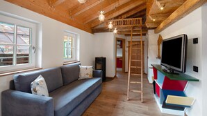 Un salon avec un canapé, une télévision, un plafond en bois et une échelle.