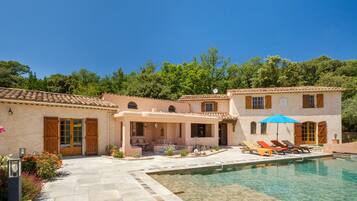 A Mediterranean-style villa with a swimming pool, outdoor seating, and a covered patio.
