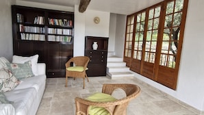 A living room with a sofa, two wicker chairs, a bookshelf, a small cabinet, and a staircase leading to an outdoor area. - Villa 'Propriété Fontaine Margo': Peaceful Retreat with Mountain Views (Seillans)