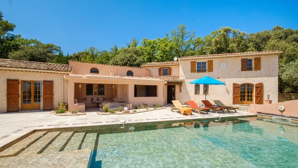 A pool with lounge chairs and a blue umbrella, a patio area with outdoor seating, and a building with a tiled roof and wooden shutters. - Villa 'Propriété Fontaine Margo': Peaceful Retreat with Mountain Views (Seillans)