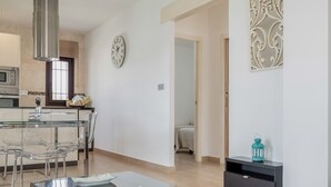 A modern kitchen with a dining area, a clock on the wall, and a decorative wall piece.