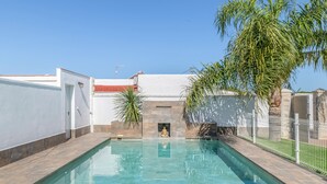 A swimming pool with a clear blue water, a white wall, and a palm tree.