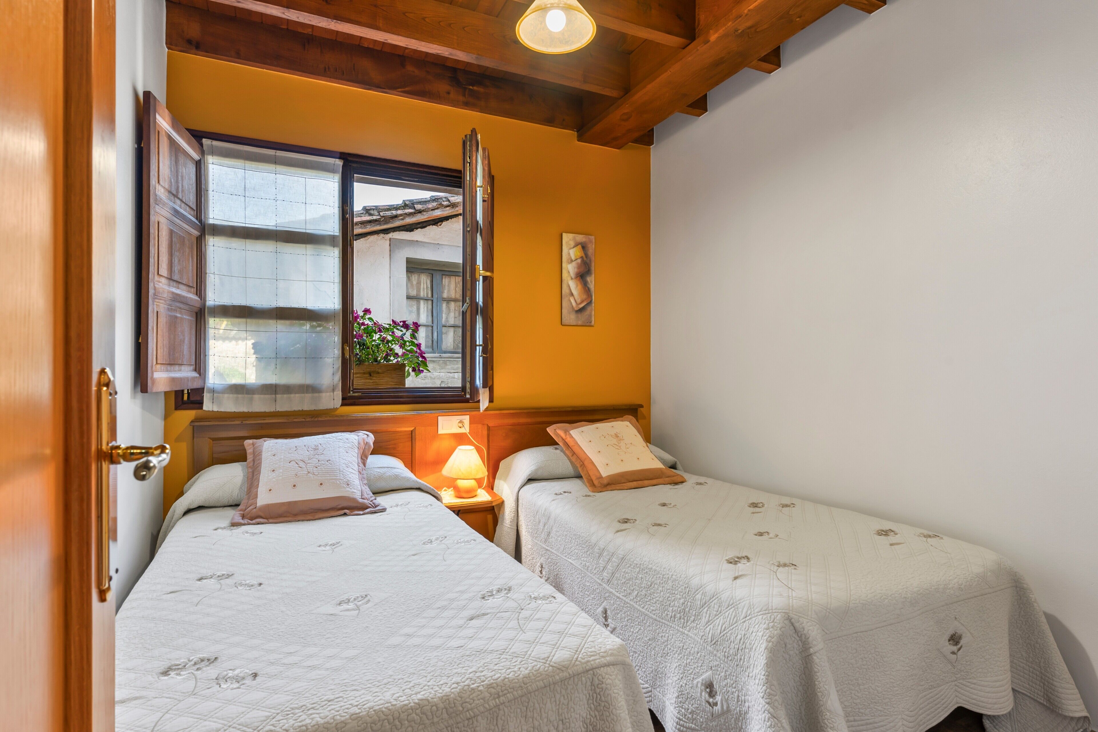 Een kamer met twee bedden, een raam met uitzicht, een lamp en een houten plafond.