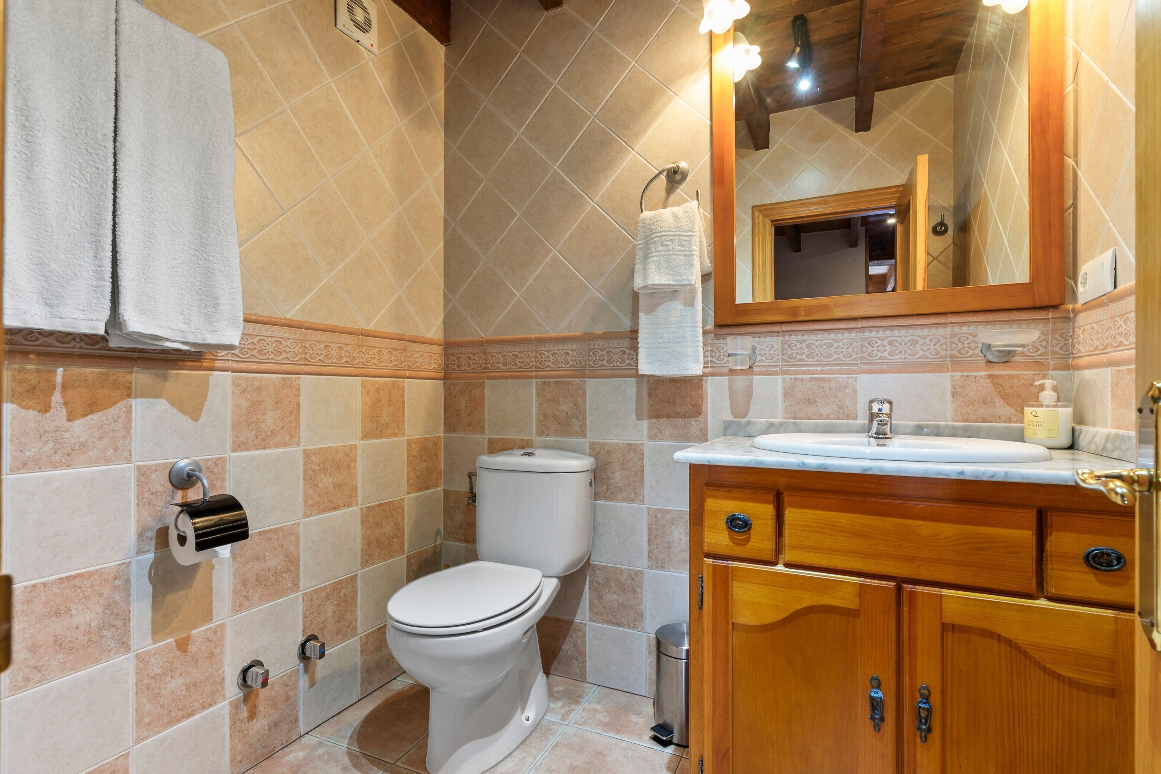 A bathroom with a toilet, sink, wooden cabinets, a mirror, and a towel rack.