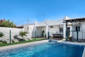 A swimming pool with a tiled edge, surrounded by a white building with a covered patio area.