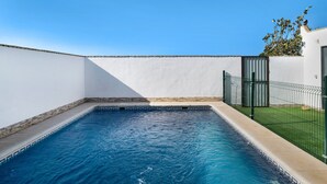 Une piscine dont le bord est recouvert de carreaux, entourée d’un mur blanc et d’une clôture en métal.