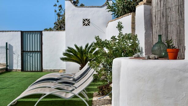 Un mur blanc avec une fenêtre, un portail en métal et une rangée de chaises longues.