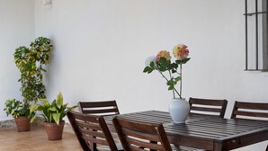 Une table à manger avec des chaises, un vase rempli de fleurs et des plantes en pot.
